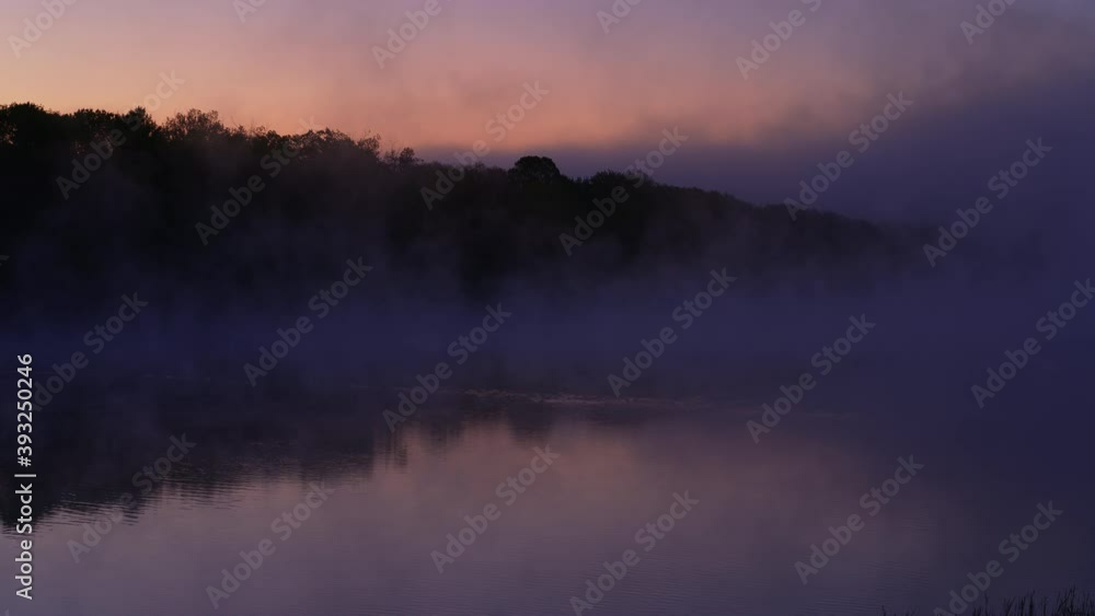 Stunning early morning shot of wide river with pink skies, and beautiful reflection with silhouetted trees and flowing purple fog Stunning early morning shot of wide river with pink skies, and beautiful reflection with silhouetted trees and flowing purple fog