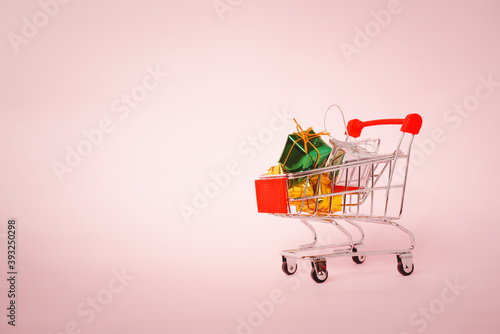 small gift boxes in miniature shopping cart on pink background with vignette