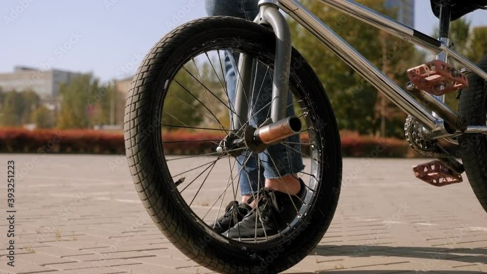 A young man walks through the Park with a BMX Bicycle, close-up of the wheel. A young man walks through the Park with a BMX Bicycle, close-up of the wheel.