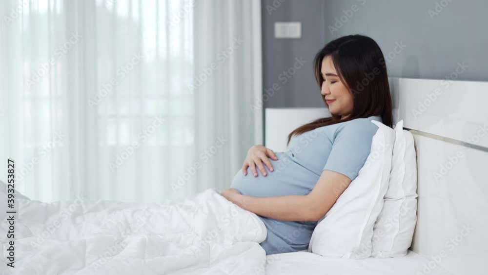 happy pregnant woman stroking her belly on a bed happy pregnant woman stroking her belly on a bed