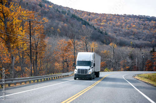 Powerful big rig semi truck with refrigerator semi trailer transporting cargo running on the winding autumn road in Massachusetts New England mountain