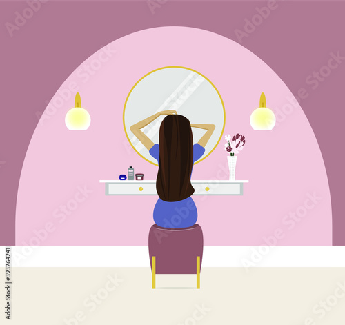 A woman with long hair preens in front of a mirror. The interior of the bedroom.