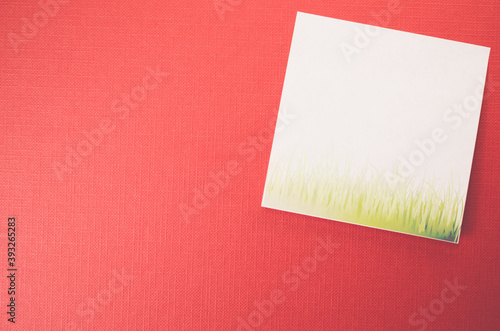 White blank memo with grass on a red textured surface photo