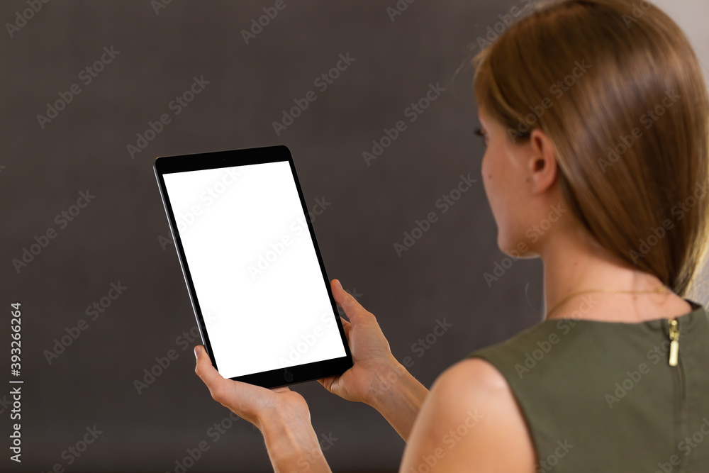 Alert female using tablet in vertical orientation and reading from white screen. Beautiful blond girl looking at black modern wireless device. Woman analyzing content from monitor.