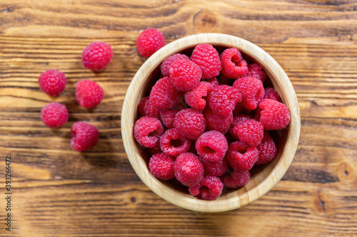 Full bowl of fresh ripe raspberries on wooden table. Pile of little red raw fruit in woody dish on textured background. Heap of nutrition healthy berries on background.