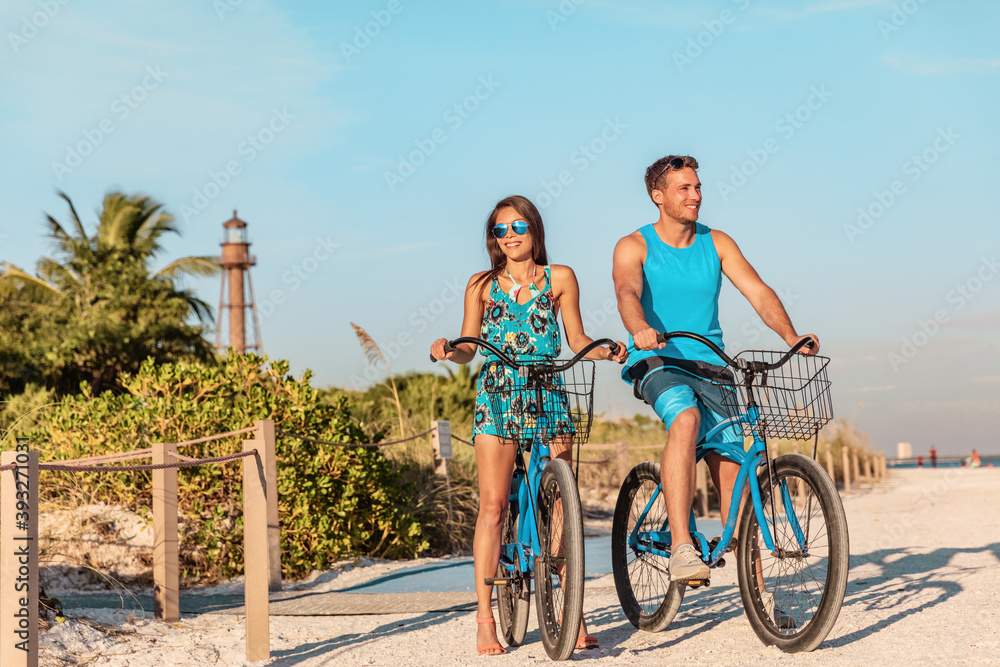 Fototapeta premium Biking activity couple tourists having fun doing outdoor sport on Florida beach vacation with rental bikes on Sanibel Island by the Lighthouse. woman with man friend riding bicycles outdoor lifestyle.