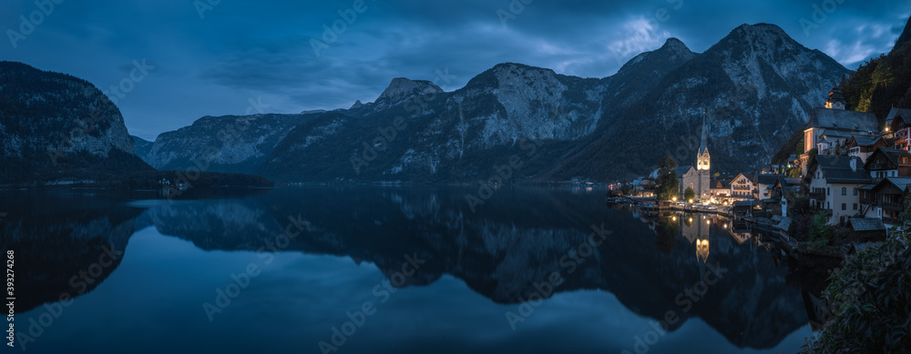 Panoramic view at the postcard angle of Hallstatt town at dusk after sunset with lake foreground and reflection, and mountain background, one of the most beautiful town in Europe