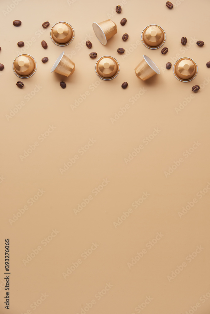Fototapeta premium Caffeine, hot drinks and objects concept - close up of golden capsules or pods for coffee mashine with some roasted grains on beige background. Top view with space for text. Flat lay..