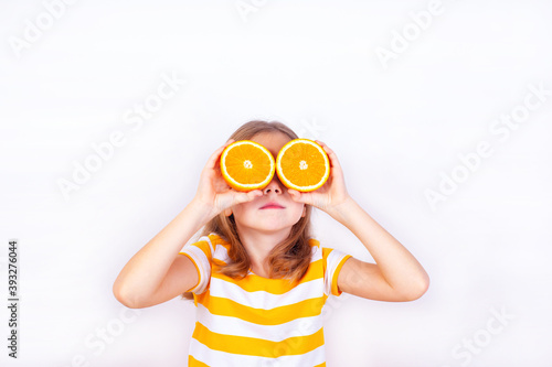A cute girl holds the orange halves to her eyes and looks up.