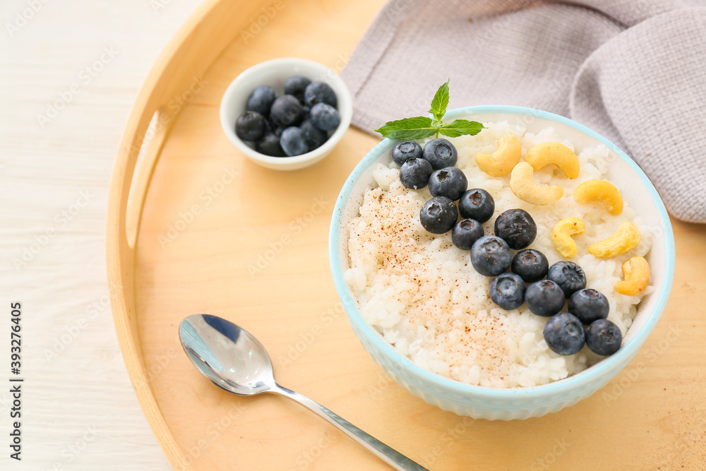 Bowl of tasty rice pudding with blueberry and cashew on wooden tray Bowl of tasty rice pudding with blueberry and cashew on wooden tray