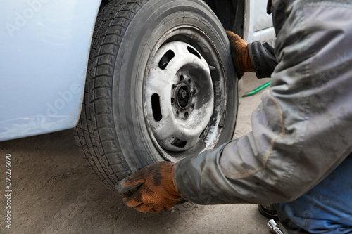 The repairman removes the wheel from the car for replacement. Seasonal change of car tires.