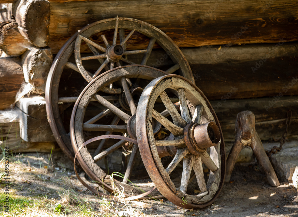 Wooden wheels from an ancient cart standing in front of the wall of a wooden country cottage