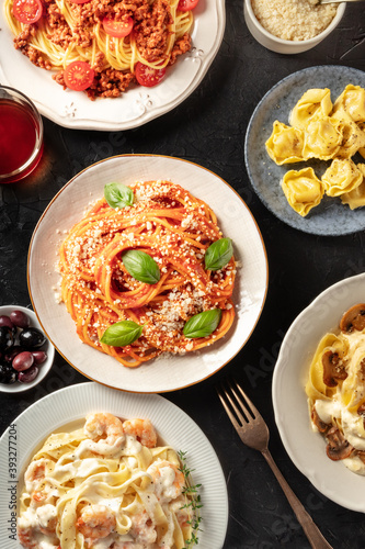 Pasta dishes variety. Pastas with meat, vegetables, seafood and mushrooms, with ravioli, grated Parmesan cheese, and wine, top shot on a dark background