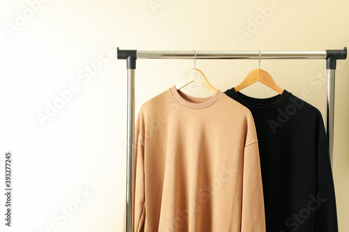 Hangers with stylish sweatshirts on beige background