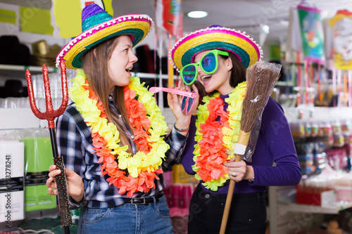 Portrait of comically dressed girls joking in festive accessories shop