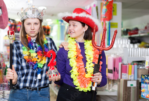 Portrait of happy comically dressed girls joking in festive accessories shop