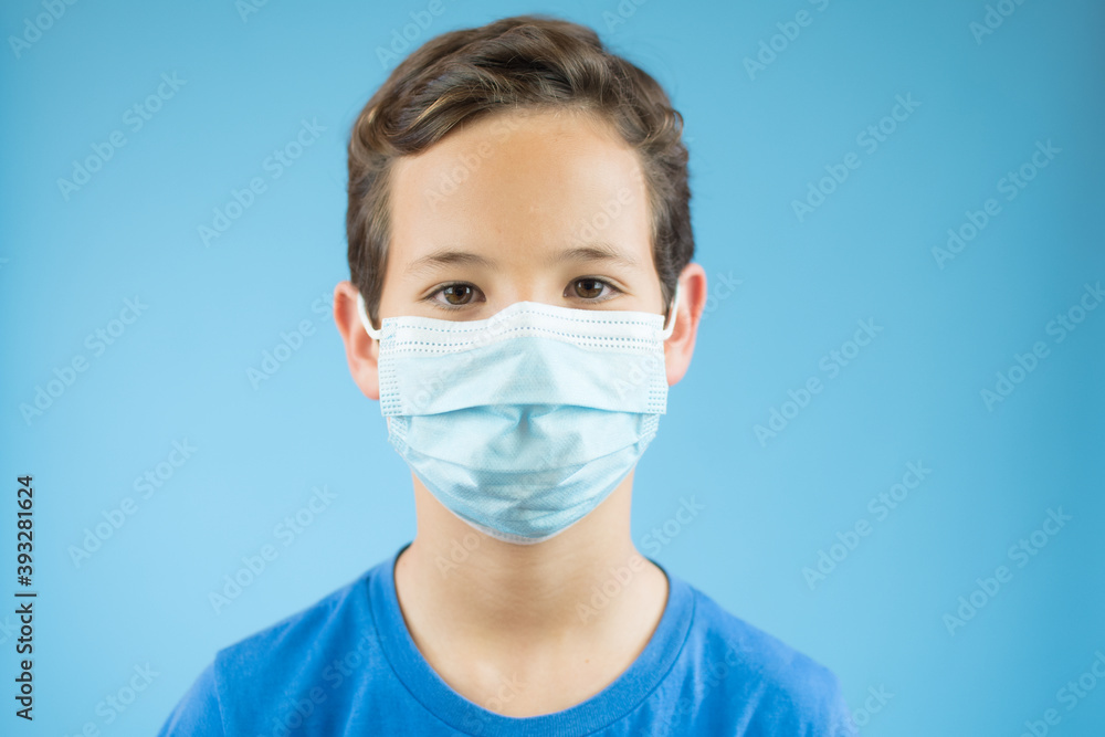 Handsome brunette boy in medical mouth mask over blue background Handsome brunette boy in medical mouth mask over blue background