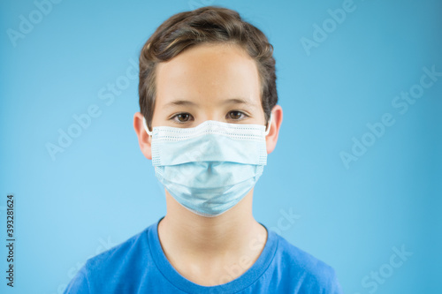 Handsome brunette boy in medical mouth mask over blue background © Danko