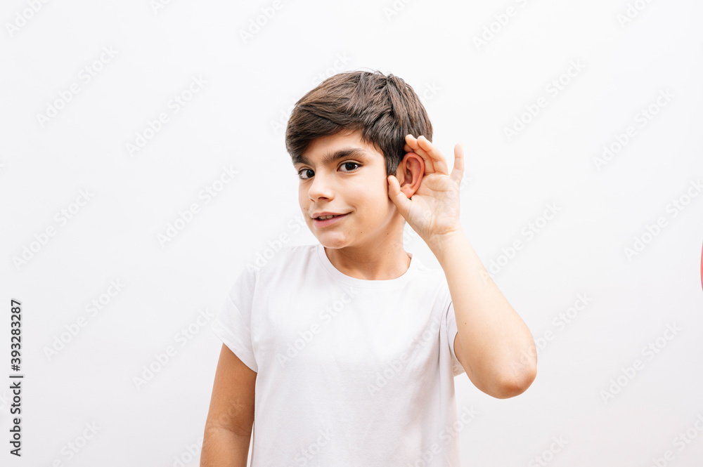 Beautiful kid boy wearing casual t-shirt standing over isolated white background smiling with hand over ear listening an hearing to rumor or gossip. Deafness concept. Beautiful kid boy wearing casual t-shirt standing over isolated white background smiling with hand over ear listening an hearing to rumor or gossip. Deafness concept.