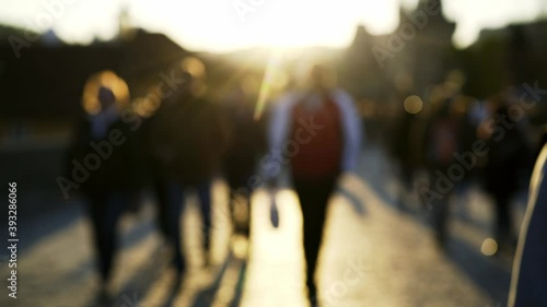 crowds of blurry local people and tourists wander along famous Charles Bridge with grey pavement under bright sunset light in spring evening 