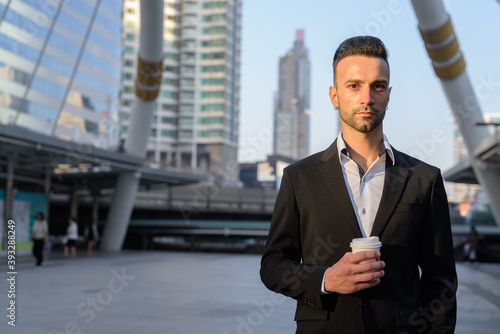 Canvas Print Portrait of handsome young businessman outdoors in city holding coffee cup
