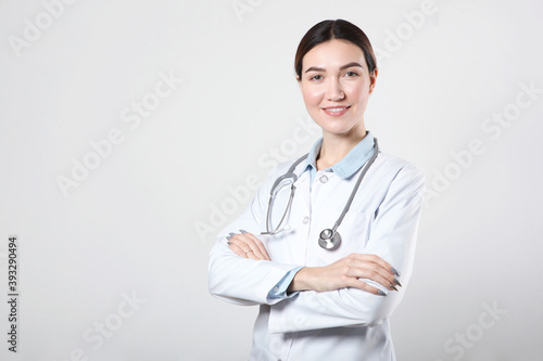 Young woman doctor on light background with place to place text