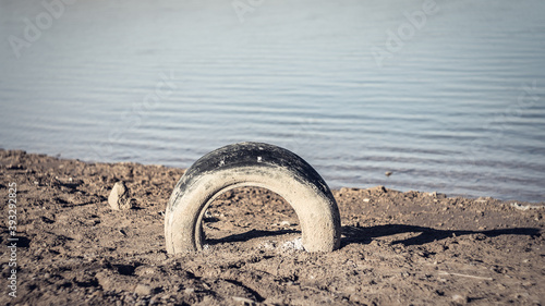 Old dirty car tire on the shore of a reservoir.