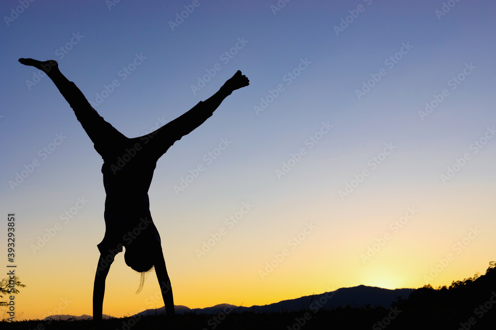 Happy child playing upside down outdoors in summer park walking on hands at sunset, silhouette Happy child playing upside down outdoors in summer park walking on hands at sunset, silhouette