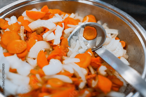 Carrots and onions are stewed in a large shiny plate on the stove. Vegetables are prepared for eating.