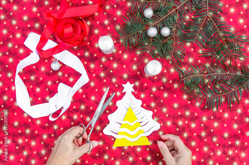Christmas background with homemade 3D Christmas tree.Hands of woman creating Christmas decoration.Xmas colorful background.Winter holiday seasonal decor.Making DIY project.Handcraft activity top view.