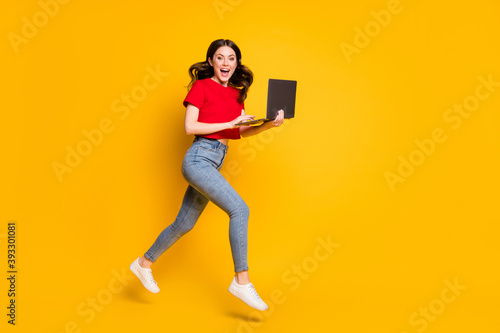 Full length profile side photo of girl work laptop internet sale jump run wear t-shirt denim isolated yellow color background