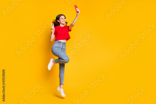 Full body photo of girl jump take selfie smartphone make v-sign wear t-shirt jeans isolated shine color background