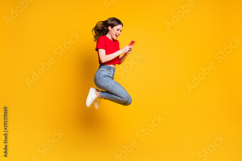 Full body photo of cheerful girl jump use smartphone discounts isolated over bright shine color background