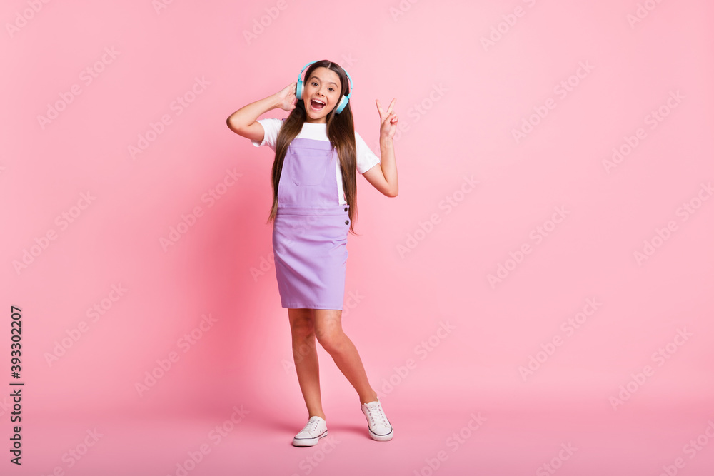 Full size photo of crazy little kid girl listen wireless headset music make v-sign wear violet skirt isolated on pastel color background Full size photo of crazy little kid girl listen wireless headset music make v-sign wear violet skirt isolated on pastel color background