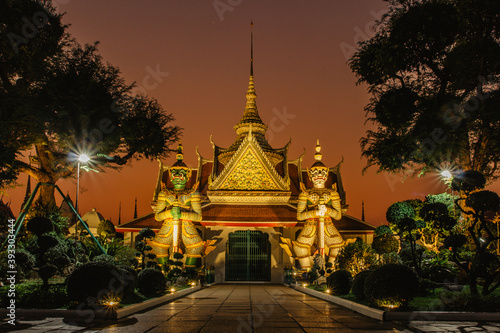 Ordination Hall next to a Buddhist temple Wat Arun in Bangkok.Thailand landmark.Colorful porcelain statues. Temple guardian figures. Night city lights. Popular tourist destination.Travel scenery.