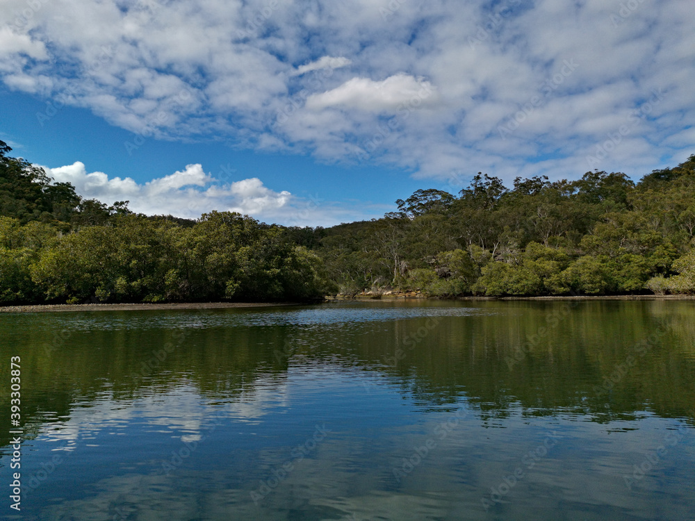 Beautiful morning view of a creek with reflections of deep blue sky, light clouds, mountains and trees, Cockle Creek, Bobbin Head, Ku-ring-gai Chase National Park, New South Wales, Australia
