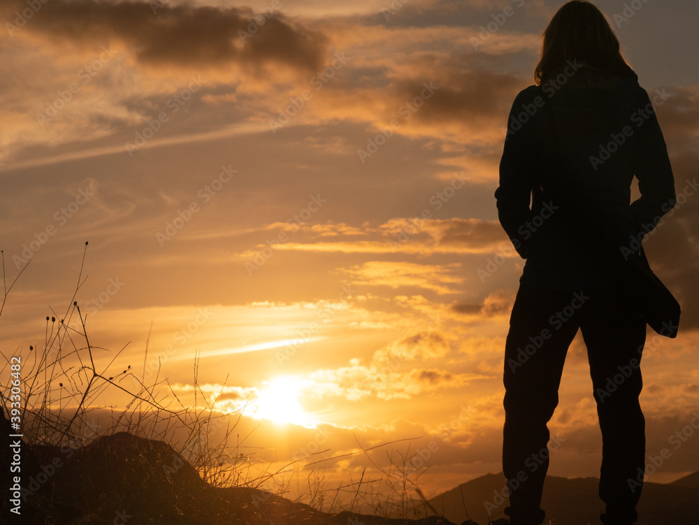 SILHOUETTE OF A WOMAN STANDING, WITH TRIPOD HANGING TO THE ESPLADA, WATCHING THE SUNSET ON A HILL IN CONSUEGRA, SPAIN SILHOUETTE OF A WOMAN STANDING, WITH TRIPOD HANGING TO THE ESPLADA, WATCHING THE SUNSET ON A HILL IN CONSUEGRA, SPAIN