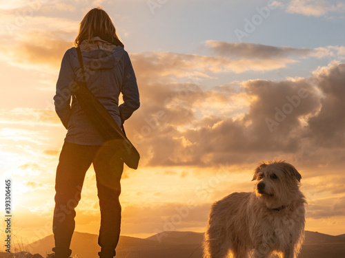 SILHOUETTE OF A WOMAN STANDING WITH DOG AND TRIPOD HANGING IN THE ESPLADA, WATCHING THE SUNSET ON A HILL IN CONSUEGRA, SPAIN photo
