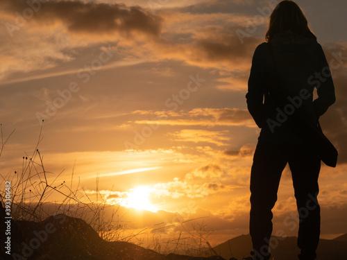 SILHOUETTE OF A WOMAN STANDING, WITH TRIPOD HANGING TO THE ESPLADA, WATCHING THE SUNSET ON A HILL IN CONSUEGRA, SPAIN photo