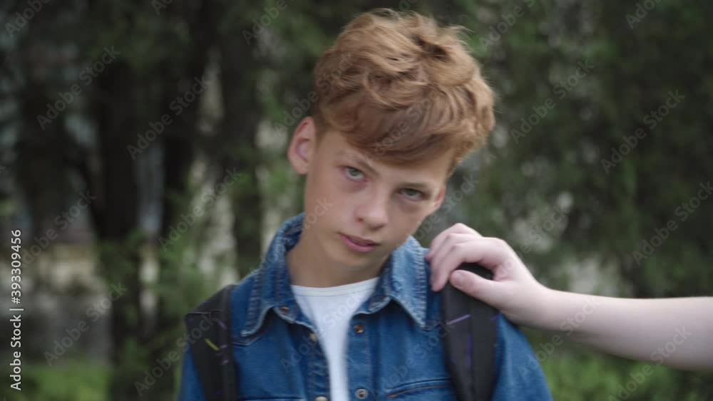 Nerd redhead schoolboy looking at camera as unrecognizable classmates pushing him. Portrait of unhappy Caucasian bullied boy on schoolyard suffering teasing. Bullying concept. Nerd redhead schoolboy looking at camera as unrecognizable classmates pushing him. Portrait of unhappy Caucasian bullied boy on schoolyard suffering teasing. Bullying concept.
