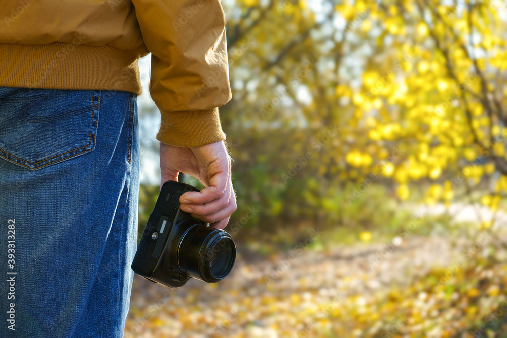 Fototapeta premium Closeup of a black camera holding by man's hand with natrural blackground in fall sunny day.