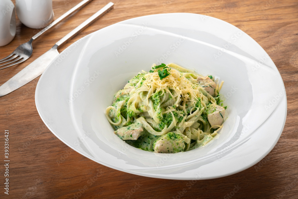 Tagliatelle pasta with pesto, chicken and Parmesan in a white plate on a wooden table