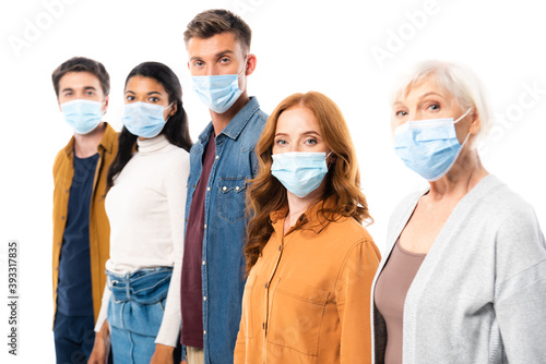 Woman in medical mask looking at camera near multicultural friends on blurred background isolated on white