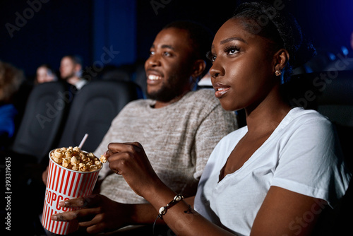 African couple eating popcorn in cinema.