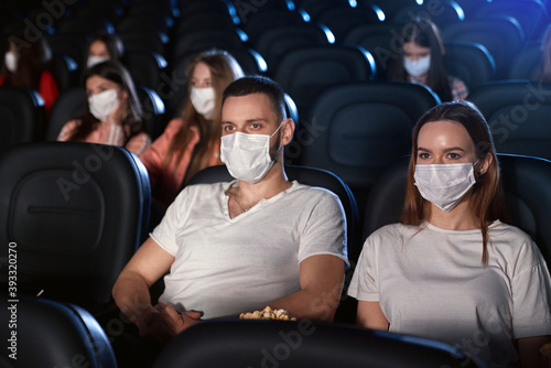 Caucasian couple wearing face masks in movie theater.