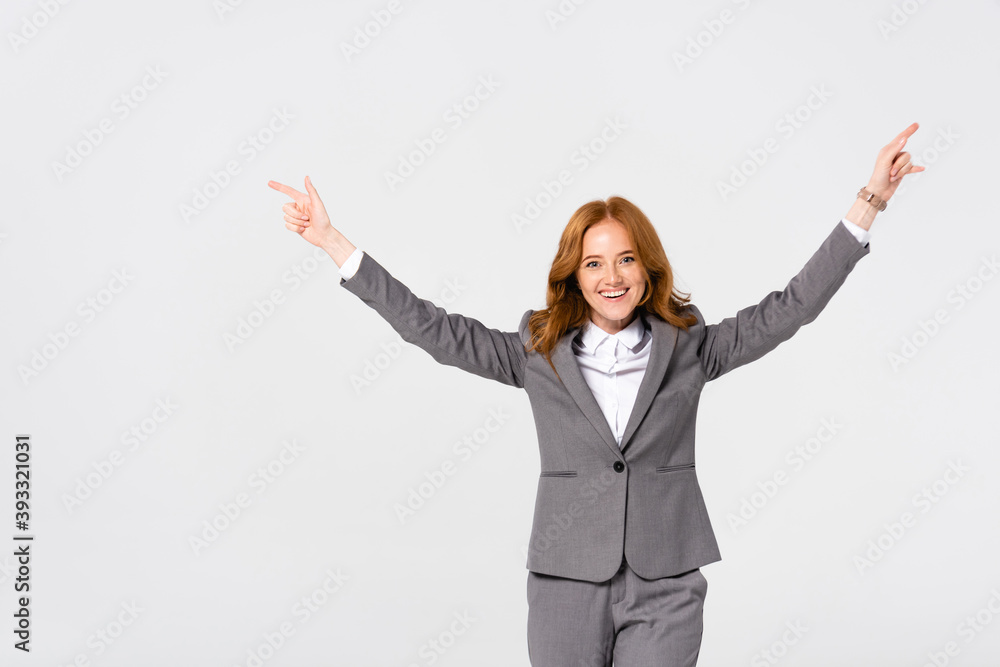 Smiling businesswoman in suit pointing with fingers isolated on grey Smiling businesswoman in suit pointing with fingers isolated on grey