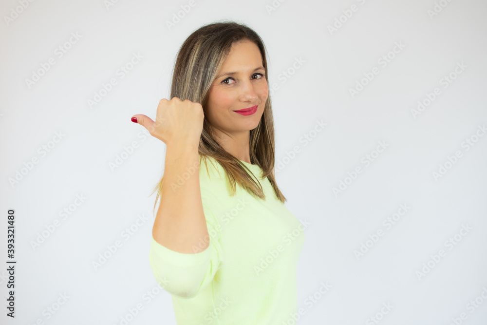Young woman over isolated white background pointing thumb to the side Young woman over isolated white background pointing thumb to the side