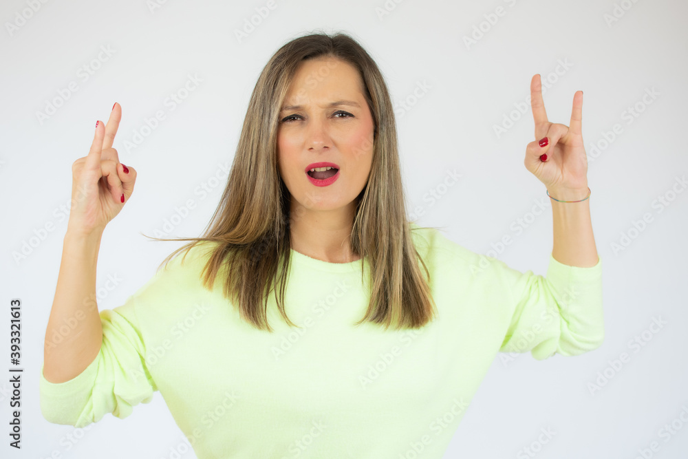 Young woman wearing casual sweater with crazy expression doing rock symbol with hands up. music star. heavy concept. Young woman wearing casual sweater with crazy expression doing rock symbol with hands up. music star. heavy concept.