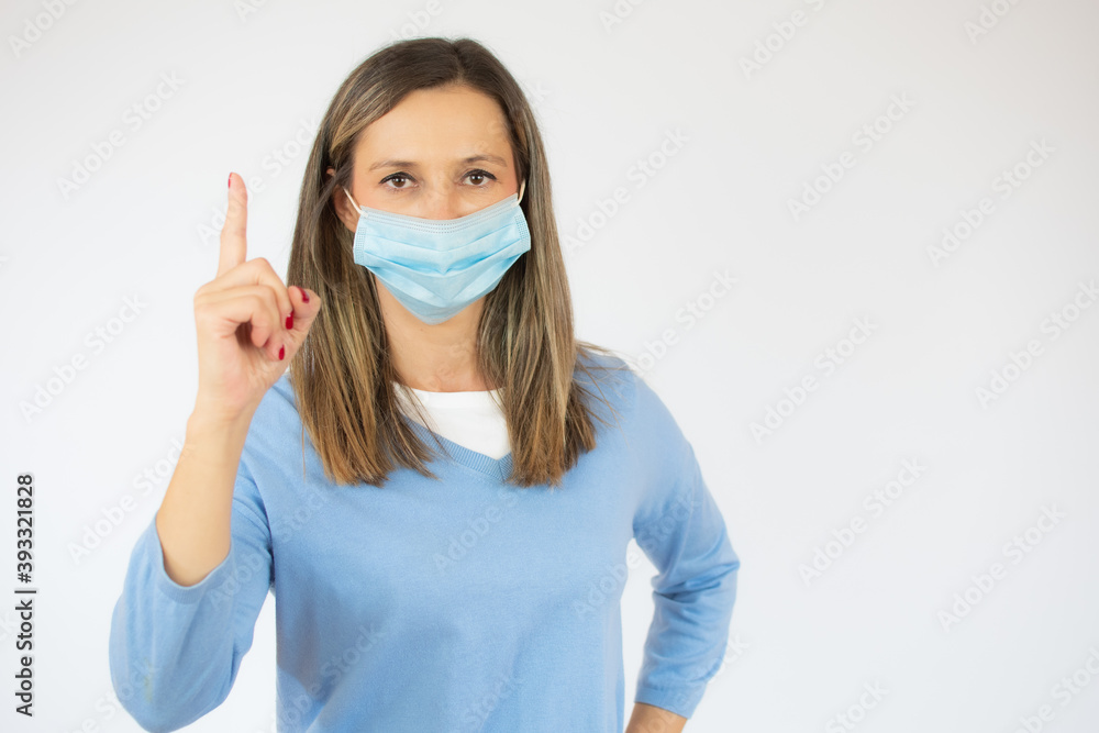 Woman wearing surgical mask pointing up finger over white background. Woman wearing surgical mask pointing up finger over white background.