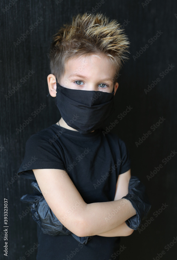 A five-year-old boy wearing a mask and gloves is protected from coronavirus. Blond boy in black medical mask against coronavirus.Boy in black mask on a black isolated background. A five-year-old boy wearing a mask and gloves is protected from coronavirus. Blond boy in black medical mask against coronavirus.Boy in black mask on a black isolated background.